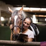 Smiling female jockey using digital tablet while standing by horse